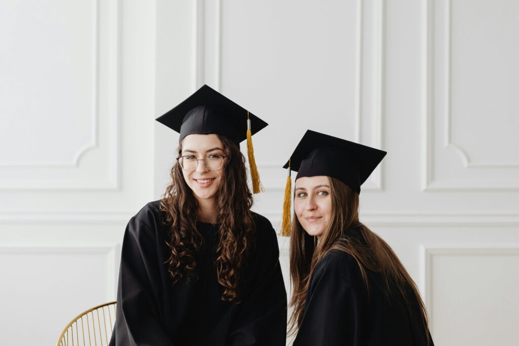 Proud female graduates wearing caps and gowns, smiling inside a bright, elegant room.